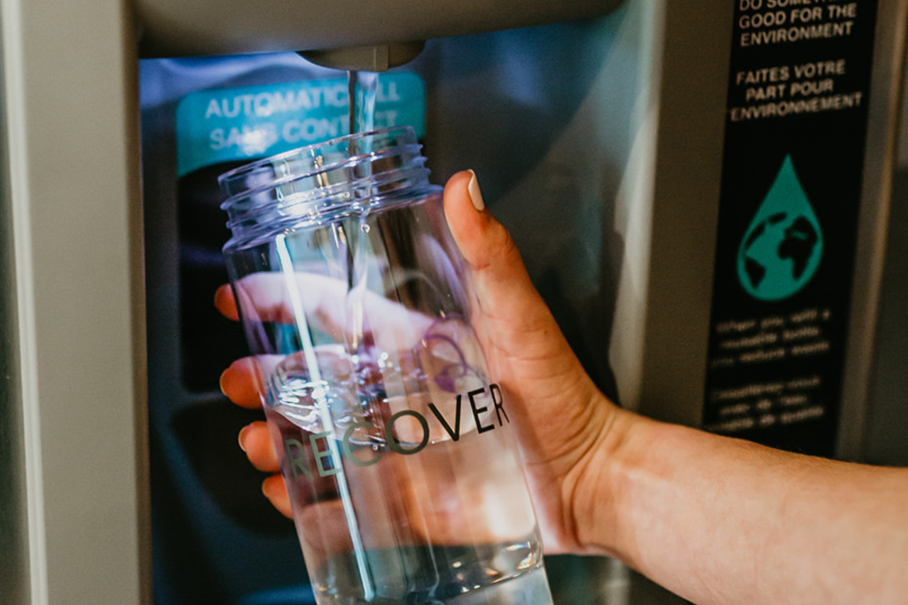 A hand filling up a Recovery Lab water bottle at a water fountain to help stay hydrated as an important part of sport recovery.