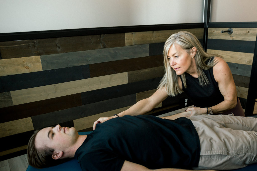 A Fascial Stretch Therapist working on a male patient's arm while he's lying down, face up