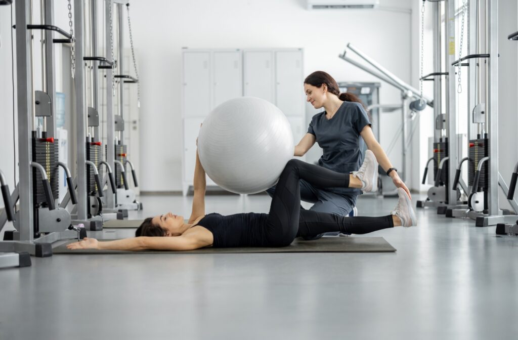 A physiotherapist helps a person train mobility and flexibility using an exercise ball.