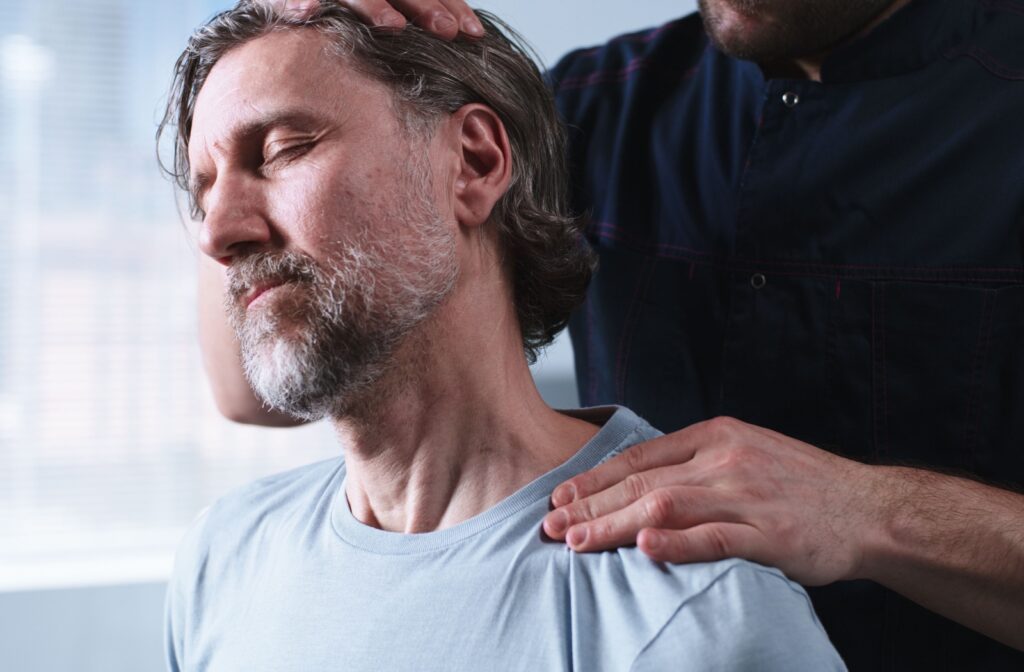 A manual osteopath gently performs a neck and shoulder assessment on a man, focusing on relieving tension and improving alignment.