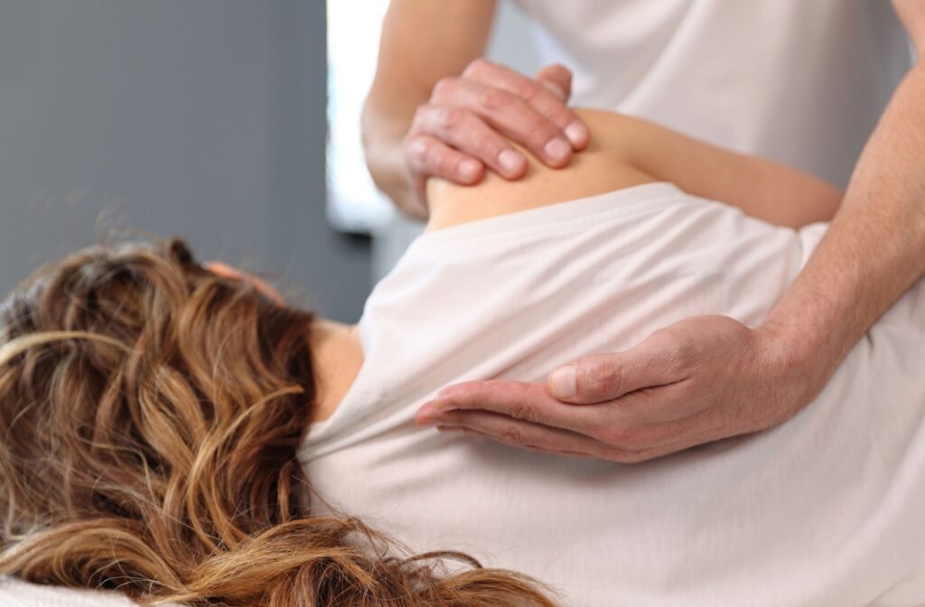 A person rests on their side, turned away from the camera, as an osteopath evaluates them.