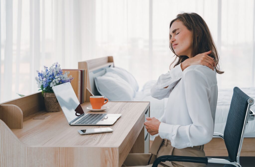 A person working at a laptop rubs at the tension in their neck.