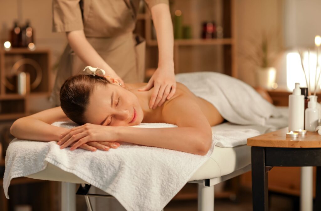 A woman relaxes during a professional shoulder massage in a warm, softly lit spa setting, surrounded by calming decor and aromatherapy candles.