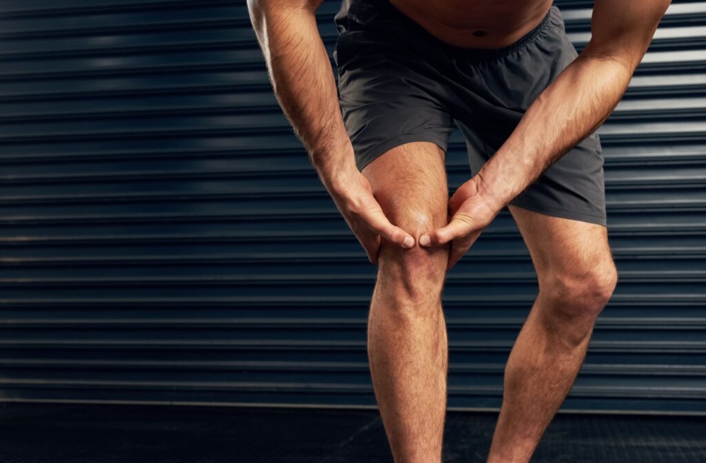 A person wearing shorts bends forward, gripping their knee with both hands, indicating ACL discomfort.