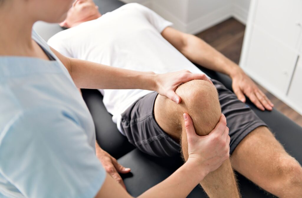 A healthcare professional gently examines the knee of a person lying on a table during a physiotherapy session.